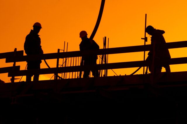 Construction workers silhouetted against an orange sky